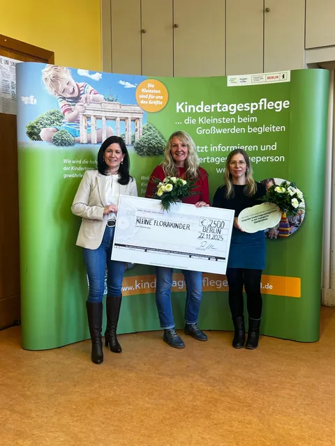 Preisübergabe vor dem Aufsteller der Berliner Kindertagespflege: das Team der Kleinen Florakinder mit Scheck und Preisschild